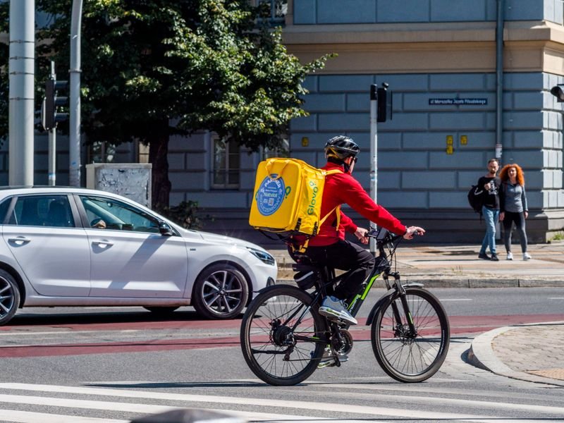 Bicycle courier with a yellow delivery backpack riding through a city intersection